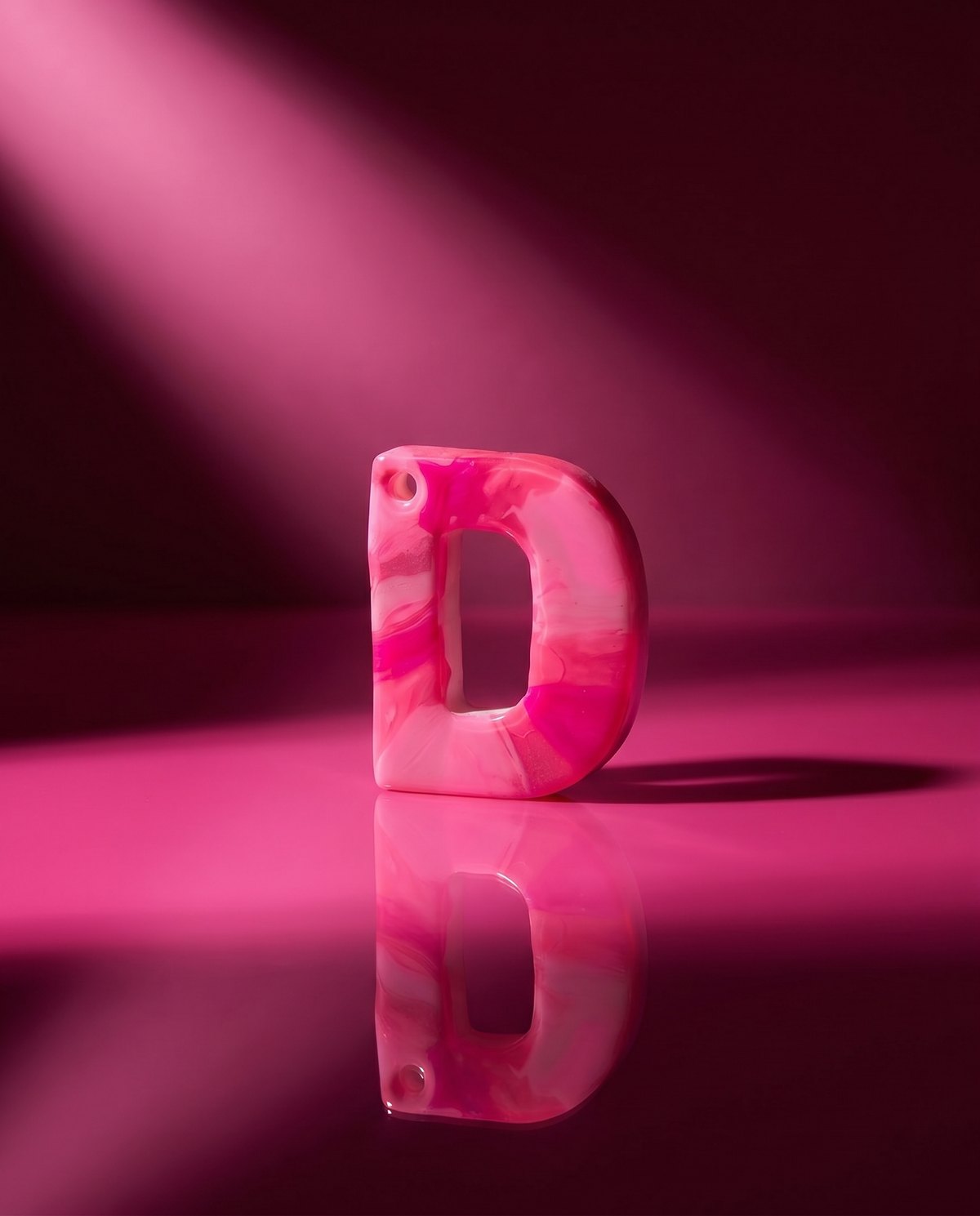 A glossy hand-painted pink marble letter D charm under a dramatic spotlight.