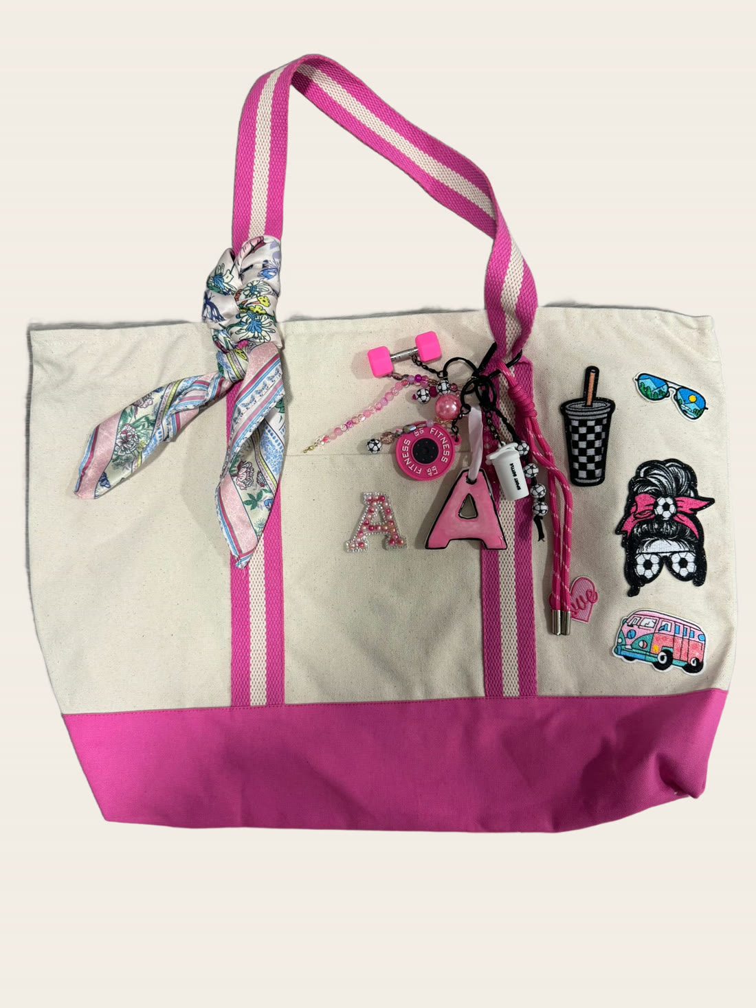 A cream and hot-pink canvas tote bag hand-decorated with an initial A patch, charms and a silk twilly scarf.