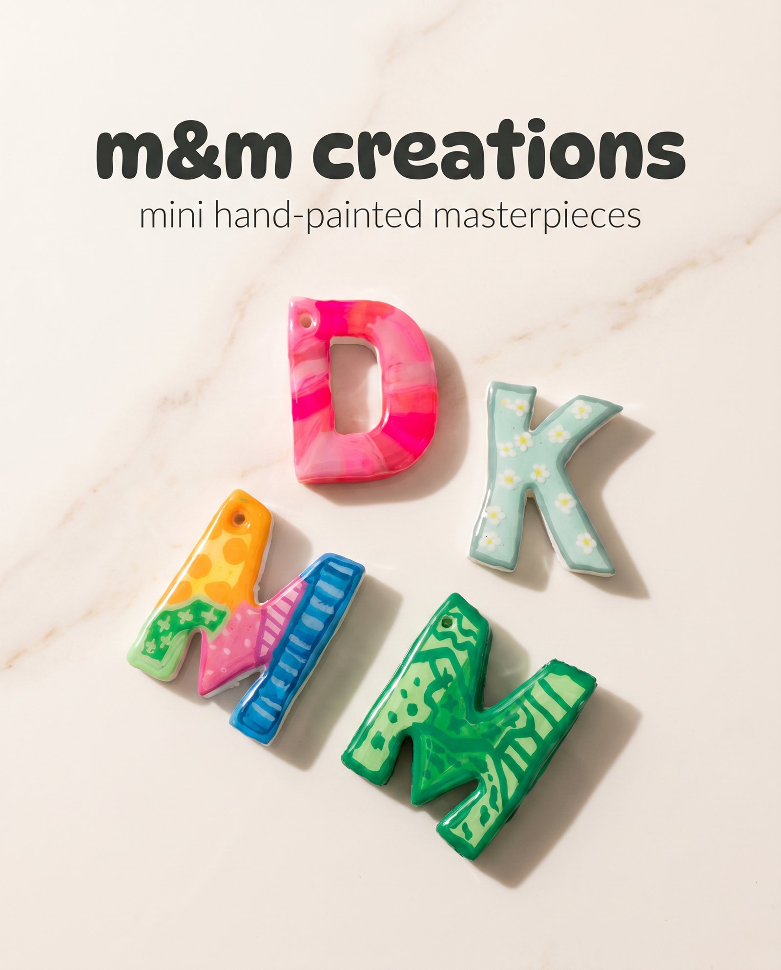 m&m creations letter charms arranged on a cream marble surface.