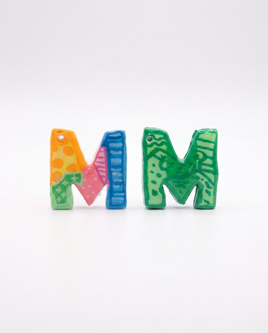 Two hand-painted letter M charms in colourful pop-art patterns.