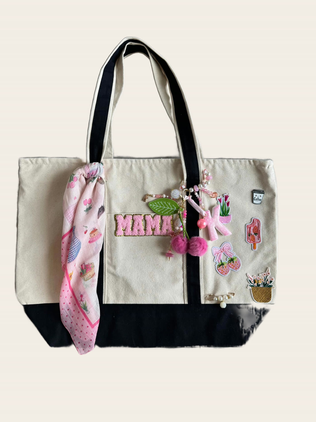 A cream and navy canvas tote with hand-stitched MAMA letters, pink charms, flower patches and a silk scarf.