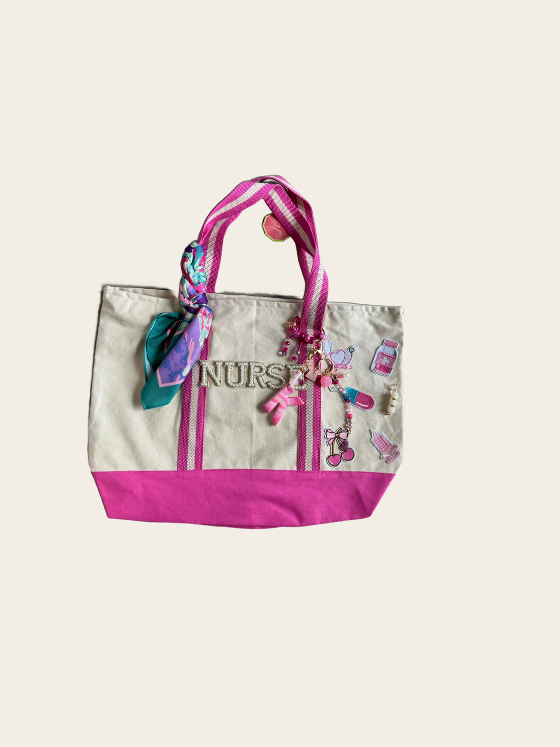 A cream and pink canvas tote with chenille NURSE letters, medical charms and a silk twilly.