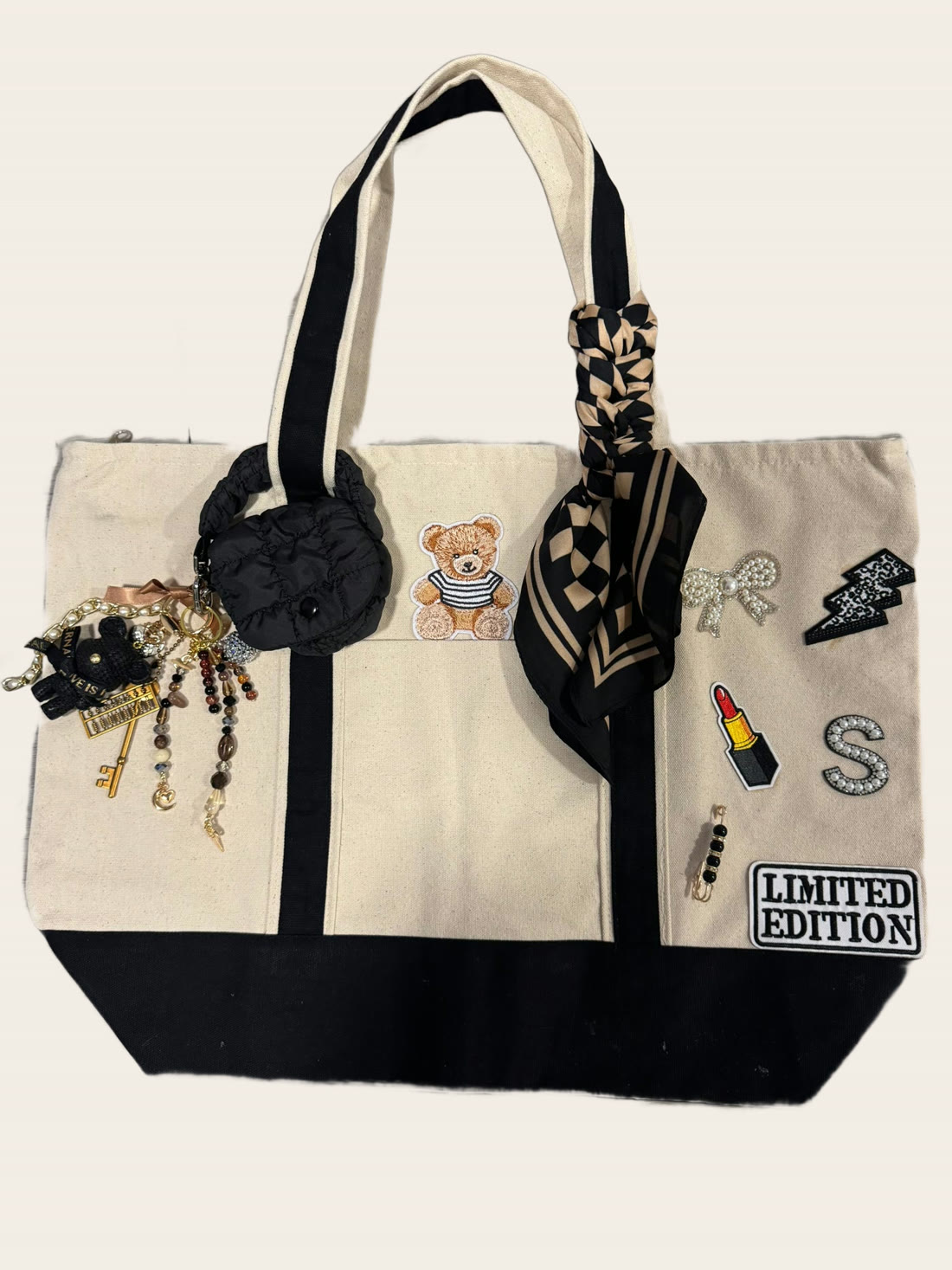 A cream and black canvas tote with a teddy bear patch, a pearl initial S, lipstick patch and a checkered twilly.